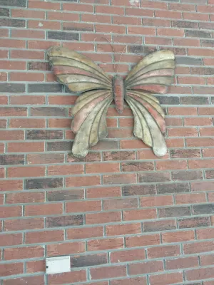 Sale Photo Thumbnail #102: Large vintage carved wood butterfly wall sculpture with painted accents, mounted on a brick wall.
