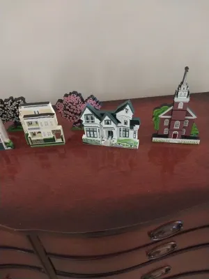Sale Photo Thumbnail #19: Collection of Cat's Meow Village wooden architectural cutouts, featuring historic homes, a church, and trees, displayed on a wooden dresser.