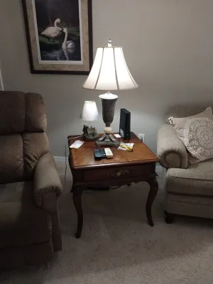 Sale Photo Thumbnail #5: Traditional wooden end table featuring cabriole legs, a single drawer, and a polished tabletop set between two upholstered armchairs. A decorative table lamp with a fabric shade and an art print of swans are displayed above and on the table.