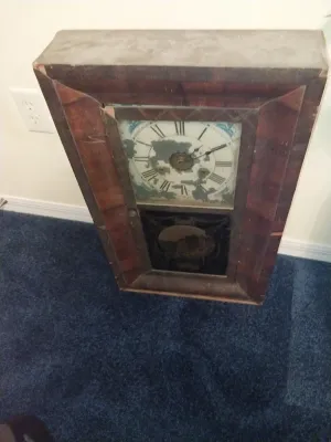 Sale Photo Thumbnail #64: Antique Ogee-style wooden shelf clock featuring a painted clock face with Roman numerals and a decorated lower glass panel, displaying significant wear.
