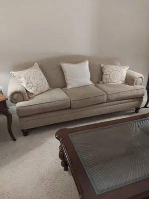 Sale Photo Thumbnail #4: Traditional beige upholstered sofa featuring rolled arms, dark wood feet, and three decorative throw pillows.