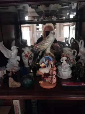Sale Photo Thumbnail #15: Collection of decorative porcelain and ceramic figurines displayed in a mirrored cabinet, featuring an eagle, bird in flight, floral vases, and a cartoon cellist bird.