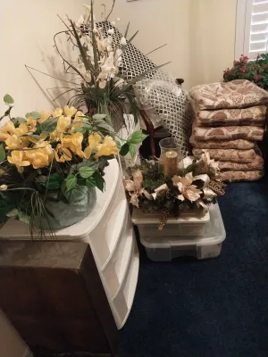 Sale Photo Thumbnail #60: Collection of artificial floral arrangements, a holiday centerpiece with hurricane glass, and a stack of patterned chair cushions.