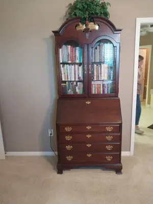 Sale Photo Thumbnail #86: Traditional dark cherry wood slant-front secretary desk with a broken-arch pediment, glass-front upper bookcase, and brass batwing hardware.