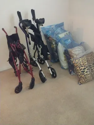 Sale Photo Thumbnail #56: Collection of mobility aids including two rolling walkers and an upright rollator, alongside bagged pillows and plush leopard-print throw pillows.