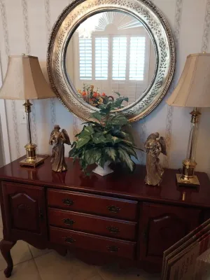Sale Photo Thumbnail #36: Traditional cherry-finished credenza featuring brass drop-pull hardware and cabriole legs, styled with a pair of brass and crystal lamps and a large round silver-finished mirror.