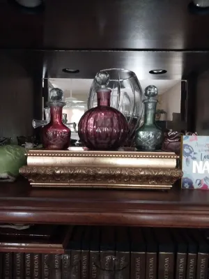 Sale Photo Thumbnail #14: Collection of decorative cut crystal and colored glass perfume bottles displayed on a gold ornate riser inside a wooden cabinet.