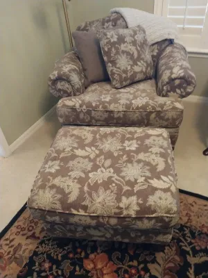 Sale Photo Thumbnail #50: Upholstered armchair and matching ottoman with a brown and cream floral Jacquard pattern, rolled arms, and accent pillows.