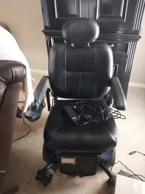 Sale Photo Thumbnail #9: Black vinyl motorized wheelchair with joystick control and included power charging cable.