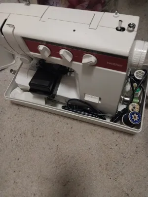 Sale Photo Thumbnail #92: Vintage Brother sewing machine in a white hard-shell base with foot pedal and assorted spools of thread.