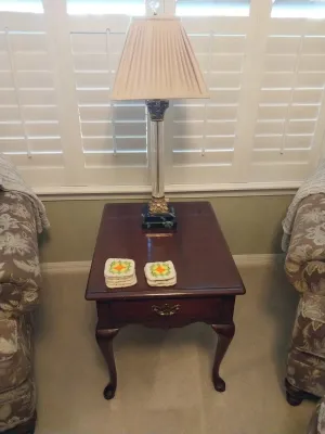 Sale Photo Thumbnail #49: Traditional dark wood end table with cabriole legs and a single drawer, topped with a brass and clear column table lamp and crocheted coasters.