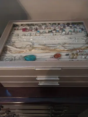 Sale Photo Thumbnail #96: Metallic champagne faux leather jewelry organizer case with glass top, filled with assortment of rings, necklaces, and earrings.