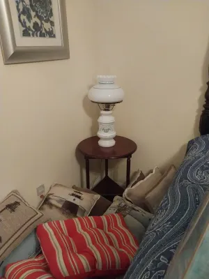 Sale Photo Thumbnail #65: Vintage white milk glass hurricane lamp with floral detail, resting on a round wooden side table surrounded by decorative throw pillows.