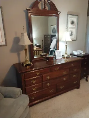 Sale Photo Thumbnail #84: Traditional cherry wood triple dresser with attached swan-neck pediment mirror, featuring brass batwing hardware and brass table lamps.
