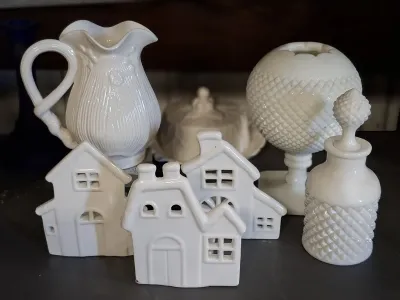 Collection of white ceramic decor, including miniature village houses, a pitcher, a milk glass vase, and a perfume bottle.