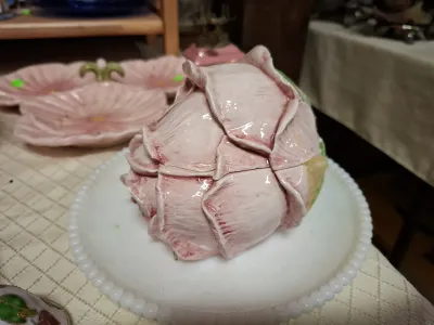 Vintage ceramic artichoke or rosebud-shaped covered box painted in shades of pink, displayed on a milk glass beaded rim plate.