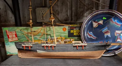 Handcrafted wooden model ship displayed alongside a vintage Paul Lindberg Shrimp Boat model kit box and a nautical decorative plate.