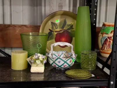 Collection of decorative glassware and ceramics featuring green art glass vases, a porcelain handled basket, a painted metal tray, and...