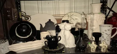 Collection of black and white home decor items, including ceramic cat figurines, a clock-face mug, a tall relief-floral vase, teacups,...