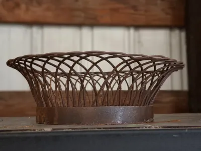 Vintage woven metal wire basket with a solid iron base and weathered rust patina.