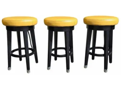 Sale Photo Thumbnail #27: Set of three modern swivel barstools featuring round mustard yellow faux leather seats and black wooden bases with circular footrests.