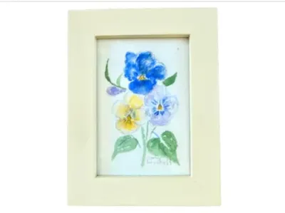 Sale Photo Thumbnail #186: Framed watercolor painting of pansy flowers in shades of blue, yellow, and purple, housed in a wide cream-colored wooden frame.