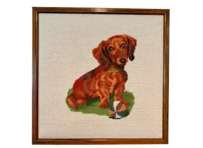 Sale Photo Thumbnail #74: Framed needlepoint art depicting a dachshund with a ball, housed in a simple dark wood frame.
