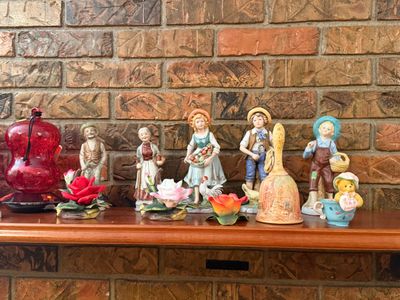Sale Photo Thumbnail #24: Collection of decorative porcelain figurines, ceramic roses, a hand bell, and a red glass hummingbird feeder arranged on a fireplace mantel.