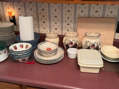 Sale Photo Thumbnail #29: Collection of country-style kitchenware featuring apple-themed bowls and plates, ceramic canisters with house motifs, plastic storage containers, and stacked dishware on a countertop.