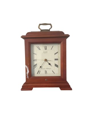Sale Photo Thumbnail #2: Seiko quartz mantel clock in a cherry wood case featuring a brass top handle and Roman numeral dial with Westminster and Whittington chimes. Shows minor cosmetic wear and paint transfer on the left edge.
