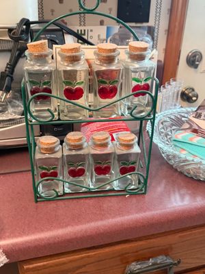Sale Photo Thumbnail #28: Vintage eight-piece spice jar set with painted red apple motifs, cork stoppers, and a green wire metal rack.