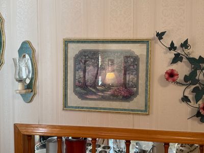 Sale Photo Thumbnail #27: Framed woodland landscape print in a gilded frame, flanked by a wall sconce and metal floral wall decor.