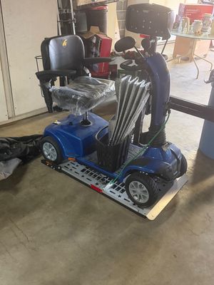 Sale Photo Thumbnail #11: Blue four-wheel Golden Technologies mobility scooter parked on a metallic ramp platform, featuring a plastic-wrapped padded seat and front storage basket.