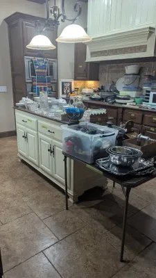 Kitchen island and folding table filled with various housewares, including crystal glassware, stainless steel mixing bowls, silver-plated...