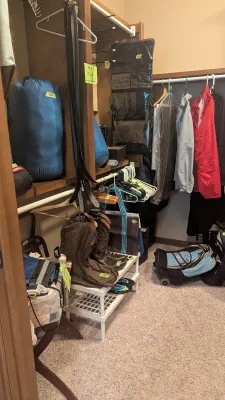 Walk-in closet featuring sleeping bags, hanging clothes, leather cowboy boots, luggage, and various accessories.