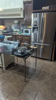 Modern stainless steel Samsung French door refrigerator displayed alongside various household goods and kitchenware on folding tables.