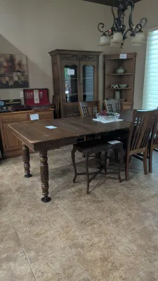 Rustic dark wood extendable dining table set with matching chairs, displayed alongside large wooden china cabinets and a side sideboard.