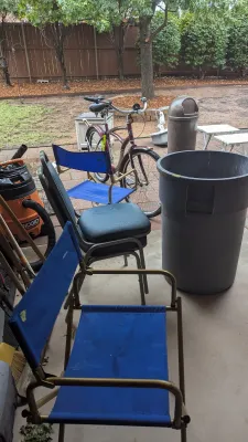 Outdoor items including blue folding camp chairs, a padded office chair, a maroon cruiser bicycle, a Ridgid shop vacuum, and a large grey...