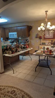 Sale Photo Thumbnail #5: Collection of rooster figurines, decorative glassware, and home decor arranged on folding tables in a kitchen area.