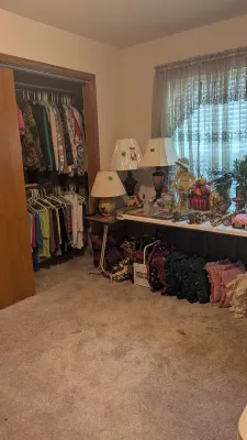 Sale Photo Thumbnail #40: Bedroom filled with estate sale items, featuring a closet full of clothing, table lamps, home decor display, and ruffled throw pillows.