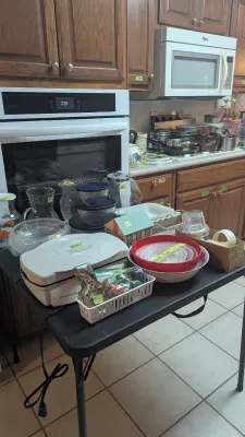 Sale Photo Thumbnail #35: Selection of kitchenware and small appliances displayed on a black folding table, including Pyrex mixing bowls, a Hamilton Beach electric griddle, glass pitchers, and food storage containers.