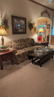 Sale Photo Thumbnail #4: Traditional floral pattern three-cushion sofa flanked by matching wooden end tables with lamps, paired with a dark wood coffee table displaying cut glass dishware.