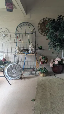 Sale Photo Thumbnail #24: Outdoor patio assortment featuring a wrought iron baker's rack, Lasko box fan, decorative plant displays, and garden tools.
