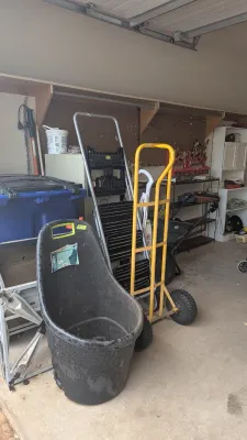 Sale Photo Thumbnail #25: Assorted garage and lawn equipment including a black plastic lawn cart, a yellow heavy-duty hand truck, and folding step ladders.