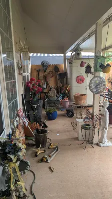 Sale Photo Thumbnail #27: Collection of outdoor and garden decor, including planters, yard tools, a utility wagon, hanging birdhouses, and a large outdoor thermometer on a covered patio.