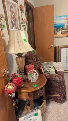 Sale Photo Thumbnail #11: A round wooden end table with a table lamp, decorative candles, and a cut glass basket, set beside a burgundy floral upholstered armchair.