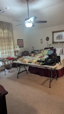 Sale Photo Thumbnail #23: Bedroom filled with estate sale items, including folding tables displays of handbags and small collectibles, alongside a white metal bed frame.
