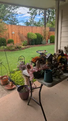 Sale Photo Thumbnail #26: Collection of outdoor and garden decor on a patio table, featuring artificial flowers, decorative birdhouses, planters, and garden accessories.