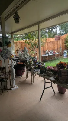 Sale Photo Thumbnail #28: Covered patio sale featuring woven wicker armchairs, garden statues, birdhouses, folding tables with decor, and outdoor planters.