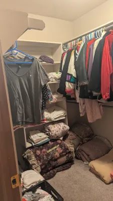 Sale Photo Thumbnail #2: Walk-in closet filled with assorted clothing including t-shirts and winter jackets, along with stacked floral comforters and folded linens.